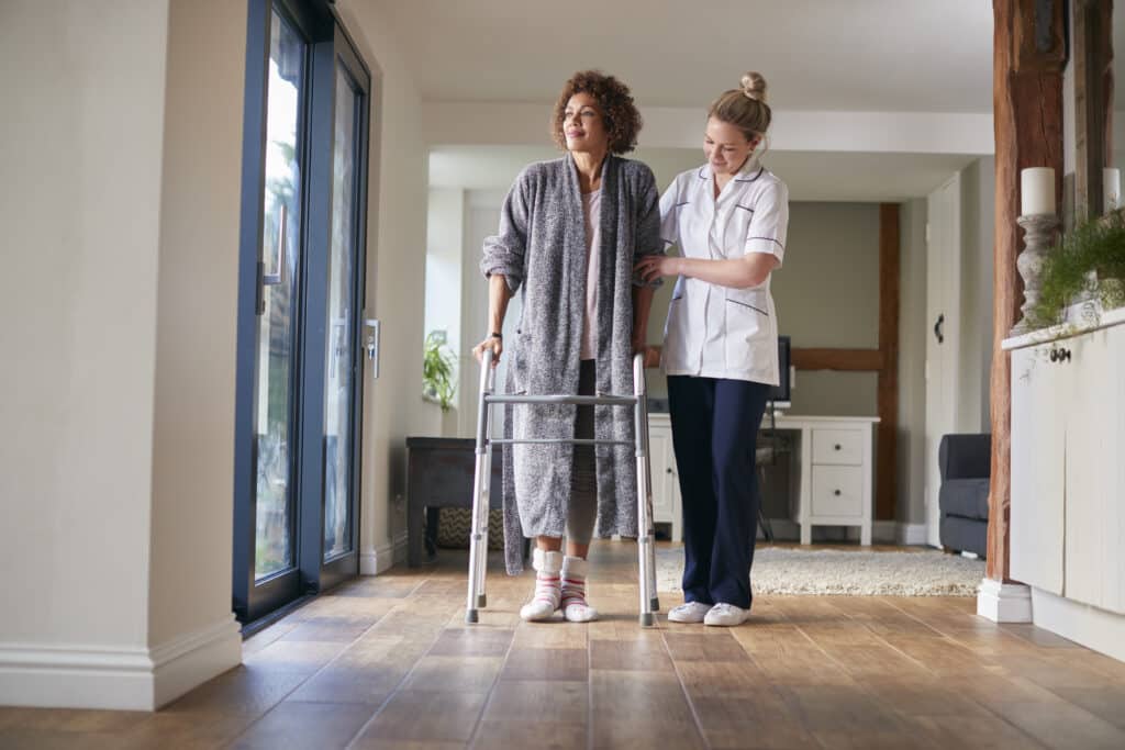 A woman with a walker and nurse in the background.